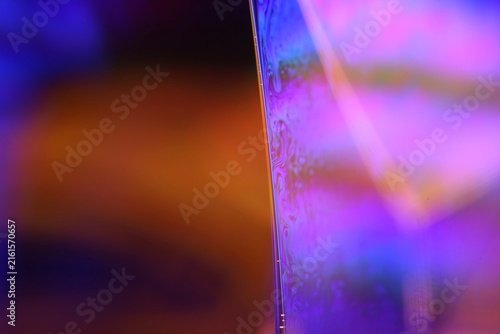 Glowing magenta and violet liquid film boundary with soft amber bokeh. Intense violet and magenta backlighting illuminates a vertical fluid plane boundary with fine suspended textures.