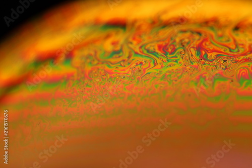 Iridescent fluid film dome with swirling rainbow interference and warm backlight. Warm golden and amber backlighting illuminates a curved fluid dome horizon.