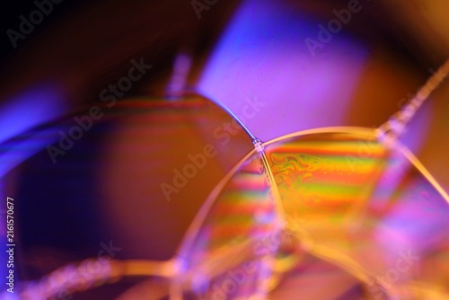 Vibrant geometric liquid film facets with rainbow iridescence. Sharp magenta-highlighted lines define an intricate geometric network of liquid film facets in a low-key macro perspective.