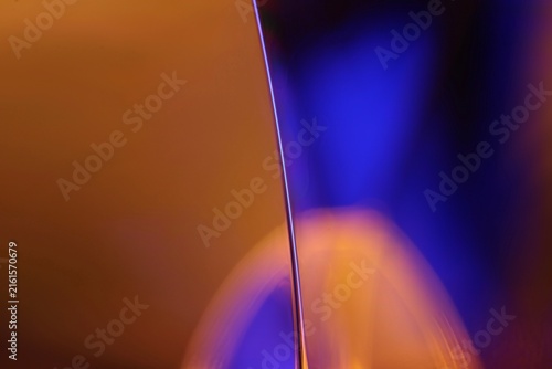 Vertical liquid film edge with warm amber lighting and electric blue bokeh. A sharp specular line highlights the vertical edge of a liquid film plane in low-key macro perspective.