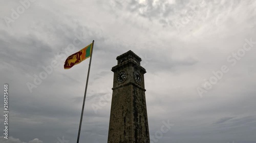 View of an old clock tower within the fortress grounds in Galle, Sri Lanka, with the national flag fluttering on a cloudy rainy daytime.