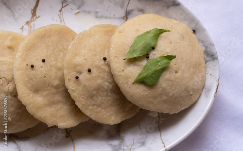 Indian idly served as a row - Fresh steamed Indian Idly (Idli / rice cake) arranged decoratively as a row on white plate, isolated on white background.