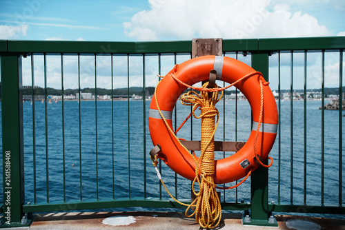 View of an orange lifebuoy with a yellow rope attached to a green metal railing overlooking the sea in Hayama, Kanagawa, Japan.