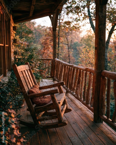 Close up view of rustic wooden rocking chair resting on cozy cabin porch overlooking vibrant colorful autumn forest during quiet morning for peaceful woodland retreat concept