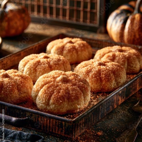 Freshly baked pumpkin shaped cookies dusted with sparkling orange sugar arranged on rustic wooden tray in cozy kitchen during autumn evening for Halloween dessert baking concept