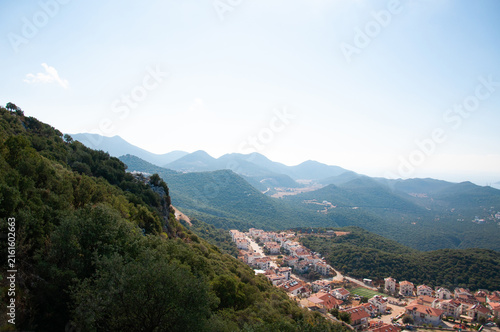 Scenic high angle view of a small mountain town with red roofs nestled in a green valley among rocky hills under a clear blue sky in Turkey