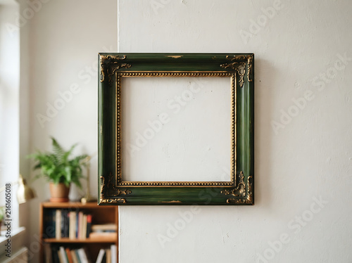 Empty vintage green and gold picture frame hanging on a white wall in a cozy home interior
