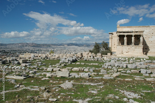 Bild auf Leinwand The ancient stone ruins of the Erechtheion temple with its iconic Caryatid porch stand overlooking the sprawling cityscape of Athens under a blue sky in Greece