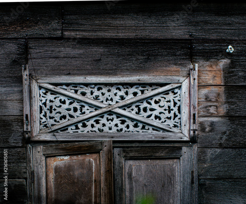 Carved Wooden Cross Pattern Transom Window on Dark Wooden Wall, Traditional Thai House Detail
