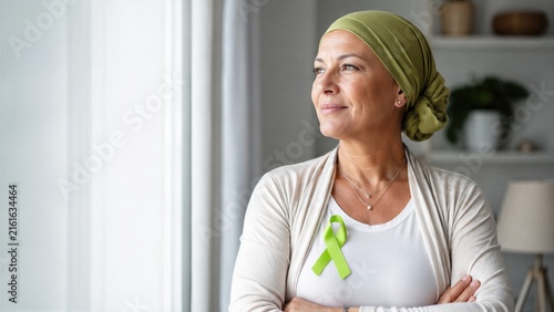 Woman cancer survivor wearing headscarf and green awareness ribbon at home. Lymphoma support, hope, treatment recovery and World Lymphoma Awareness Day concept with copy space.