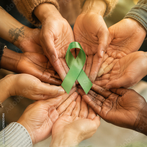 Diverse group holding a green awareness ribbon in supportive hands. Community solidarity for lymphoma awareness, cancer advocacy, healthcare education, and World Lymphoma Awareness Day.