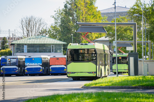 Green electric bus connected to top down pantograph fast charger at public transit depot representing clean energy urban mobility infrastructure