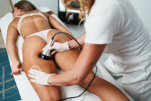 Professional cosmetologist using a modern radiofrequency machine for skin tightening and fat reduction procedure on a client body in a spa salon.