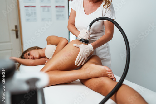Professional cosmetologist using a modern radiofrequency machine for skin tightening and fat reduction procedure on a client body in a spa salon.