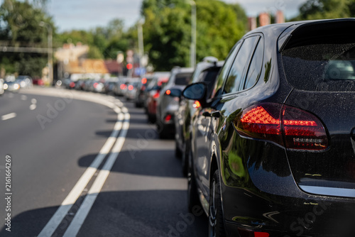 Rear focus on a dark automobile in a congested line of vehicles stopped on an asphalt road during peak commute hours