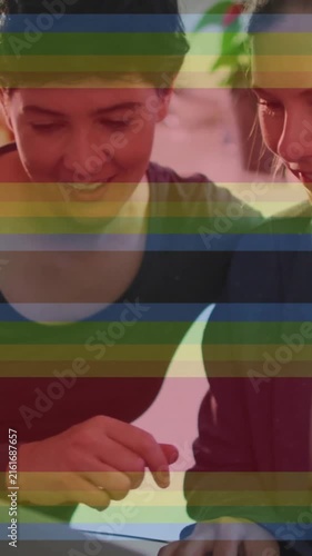 Animation of pride rainbow stripes over happy caucasian lesbian couple using laptop at home
