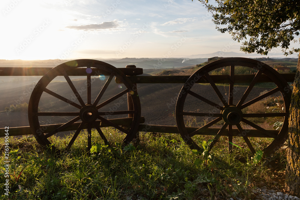 Fototapeta premium Old wooden wheels lean against a fence in a Tuscan landscape