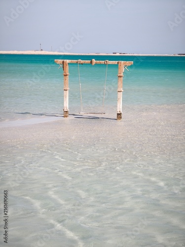 Фотография Balançoire en bois dans l'eau turquoise d'une plage tropicale