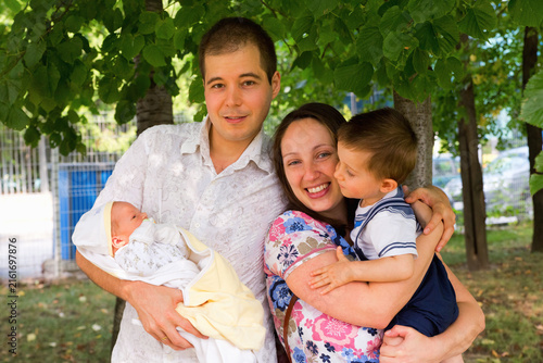 Family portrait of husband, wife, 1 year old kid and newborn baby boy shot outdoors