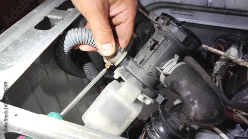 Man repairing washing machine drain hose at home, close-up of hands disconnecting white corrugated water hose from connector.