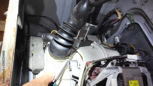 Man repairing washing machine internal motor and pump components at home, close-up of hand inspecting black mechanism with wiring.