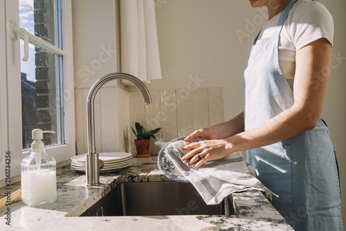 Bright kitchen scene with a person wiping dishes while standing at the sink