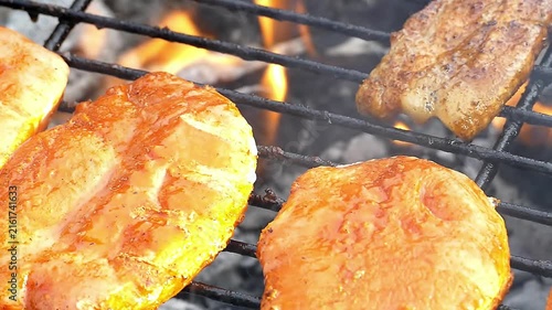 Close-up of seasoned pork belly slices sizzling on hot BBQ grill outdoors with smoke and flames