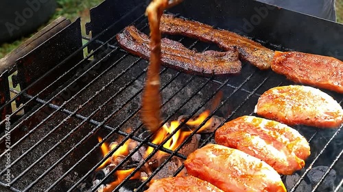Close-up of seasoned pork belly slices sizzling on hot BBQ grill outdoors with smoke and flames