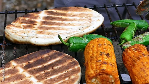 Grilling sweet corn, pita bread, and green chili peppers on barbecue grill close-up