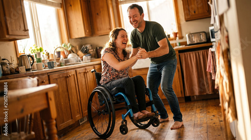 Couple laughing and dancing in a kitchen with one person in a wheelchair