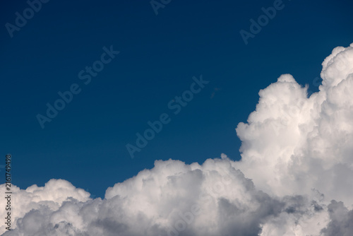 Deep blue sky with fluffy white cumulus clouds along the bottom edge. Horizontal cloudscape with ample copy space, vibrant natural light, dramatic atmosphere, clear weather, and scenic day background.
