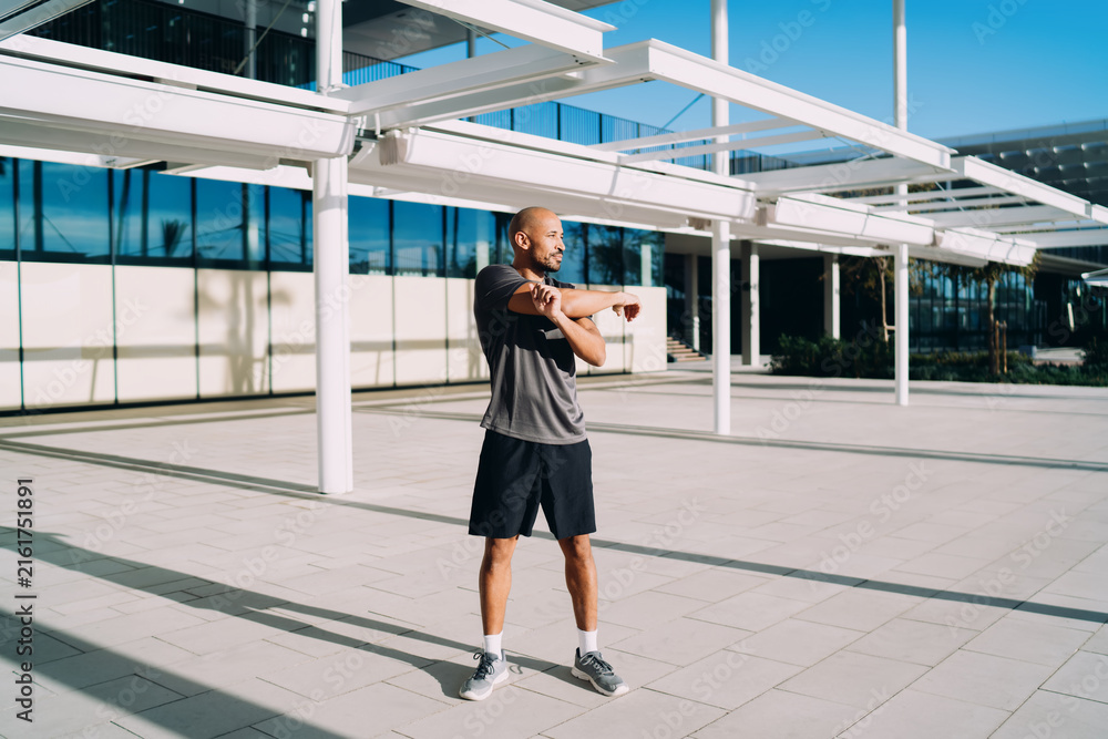 Fototapeta premium Black athlete stretching arms outdoors, muscular man warming up before workout on city plaza, healthy lifestyle, fitness motivation, authentic representation, full length, copy space, real people.