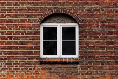 White window in old red brick wall. Arched masonry detail above modern frame. Traditional building facade texture. Historic architecture and renovation. Urban residential housing background.