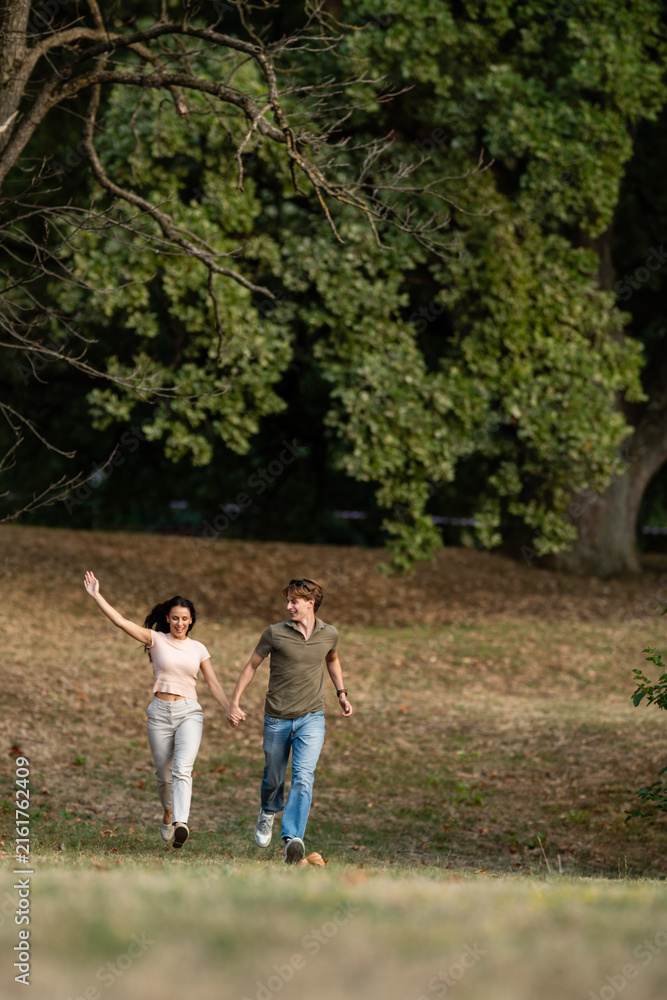 Fototapeta premium Happy couple running holding hands in park enjoying freedom