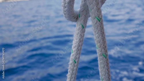 Marine rope and ocean background.
A close-up view shows a thick braided white rope hanging against a softly blurred  ocean surface. 