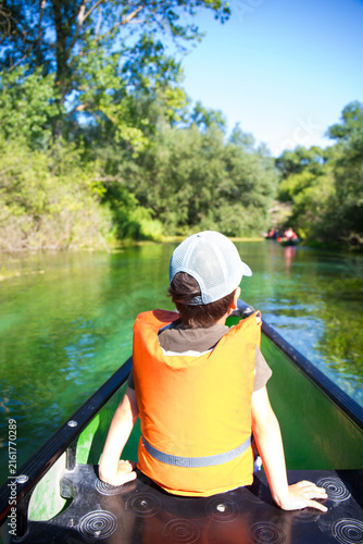 Caucasian child boy, 5 years old, with cap and life jacket, sitting on a canoe trip on Tirino River, in Gran Sasso National Park, located in the Abruzzo region in Italy