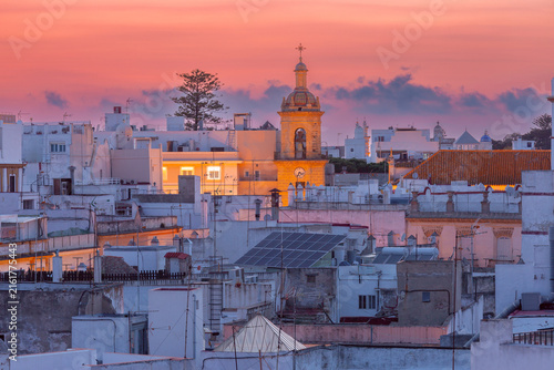 White rooftops and an illuminated bell tower under a colorful sunset sky in the historic center of Cadiz, Andalusia, Spain.