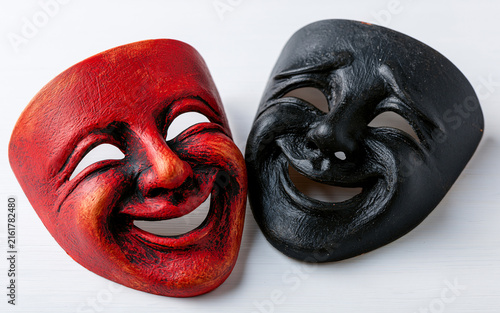 Two theatrical masks, one red and one black, with smiling faces symbolize joy and sorrow. Dramatic art faces express emotions, duality of human nature.