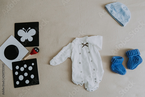 cotton baby bodysuit with soft plush knitted socks, hat, rattle and black and white cards on light beige background. Infant onesie mockup. Gender neutral newborn bodysuit template mock up. Top view