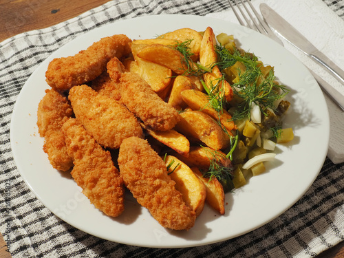 Bild auf Leinwand Golden brown fried chicken tenders sit beside crispy potato wedges on a white plate