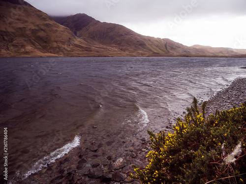 Bild auf Leinwand Gravel shore meets calm lake under cloudy sky
