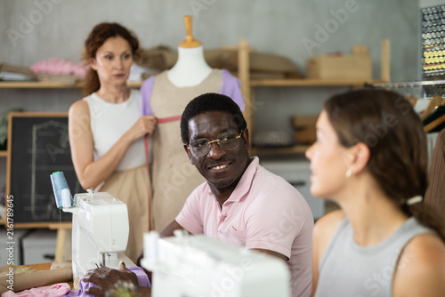 Photography Kind middle-aged male sewer speaking to woman and other measuring dummy during s