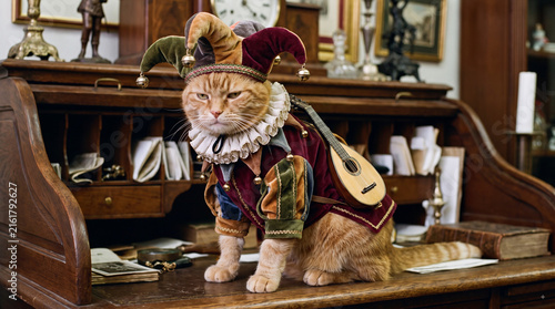 Jester Cat's Curious Pose: A ginger cat adorned in a colorful jester costume sits on a vintage desk, holding a lute, with a whimsical and intriguing expression.
