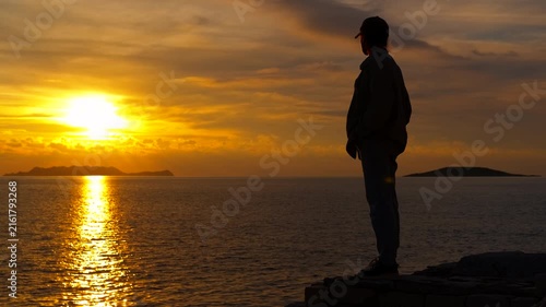 Silhouette of a woman watching the sunset over the ocean. Lone woman silhouetted against a golden sunset, standing on a cliff edge and contemplating the beautiful ocean view with the sun reflecting