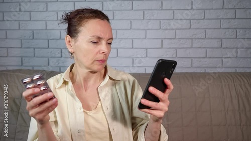 Mature woman buying medicine online using smartphone. Worried mature woman holding a blister pack of pills and looking up information about medication on her smartphone, seeking dosage instructions