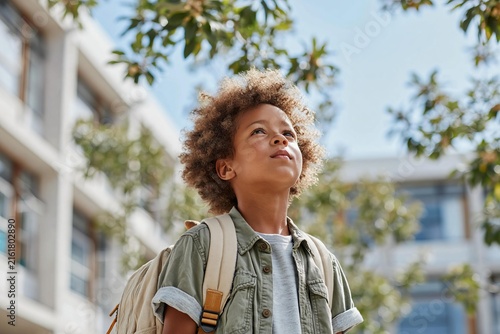 Curly hair boy looking up backpack sunny day school