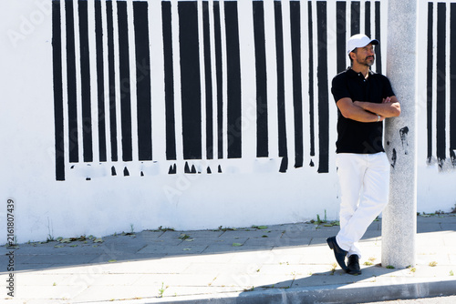 Obraz na plátně A tall, stylish, dark-haired, thin, 40-year-old white man with a beard is wearing white pants, black shoes, a black polo shirt