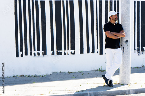 Canvas Print A tall, stylish, dark-haired, thin, 40-year-old white man with a beard is wearing white pants, black shoes, a black polo shirt