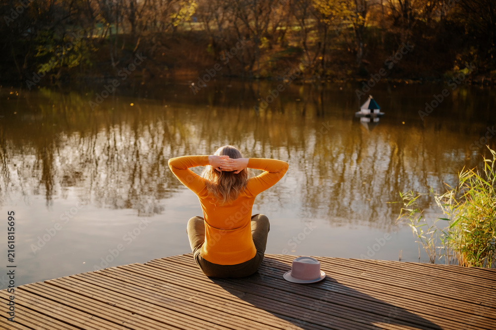 Fototapeta premium Woman traveler from back on wooden dock at autumn lake Concept of relaxation peaceful outdoor recreation mental health recovery