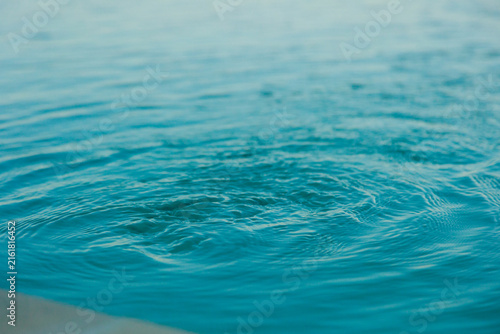 Abstract close-up of clear turquoise blue water with gentle ripples and subtle wave patterns. Minimal natural background with soft focus and vibrant aquatic tones, ideal for concepts related to water,